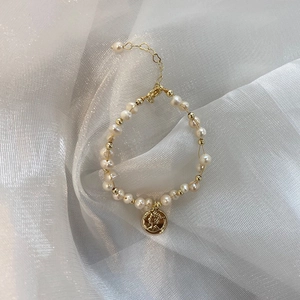 Detail of freshwater pearl bracelet with irregular pearls and a golden queen coin charm
