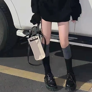 Street style view of grey over-the-knee socks with black platform shoes and beige handbag