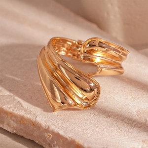 Detailed view of gold wide cuff bracelet with wavy textured metal on stone surface