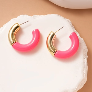 Detail of C-shaped gold metal and pink acrylic earrings on a white stone base