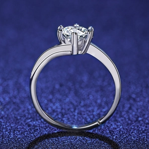 Macro side view of six-prong moissanite ring with silver bypass band on blue background