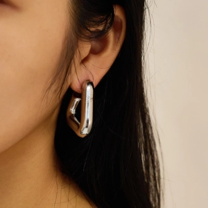 Close-up of a silver geometric triangular hoop earring worn by a female model