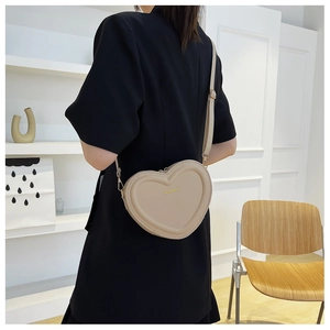 Détail du sac bandoulière beige en forme de cœur avec finitions dorées et logo texte