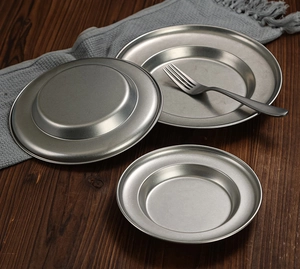 Three vintage stainless steel pasta plates and a metal fork on a dark wood table