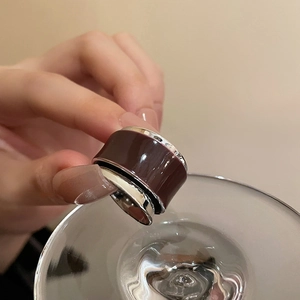 Detail of wide burgundy enamel ring with silver edges held against a glass rim
