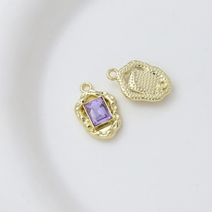 Macro detail of gold alloy charm with purple zircon inlay and textured irregular edge