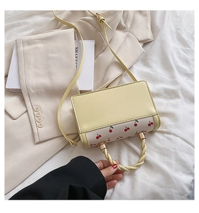 Detail of yellow cherry print handbag with twisted handle on white textured fabric
