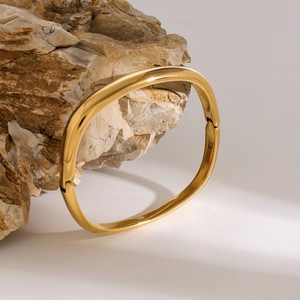 Dettaglio del bracciale quadrato dorato lucido appoggiato a una pietra naturale