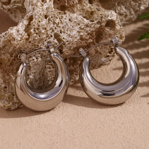 Polished silver C-shaped hoop earrings on textured surface with natural shadows
