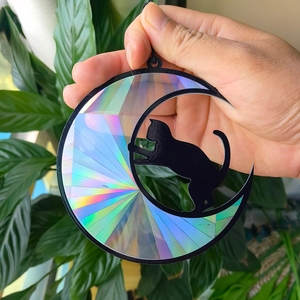 Close-up of holographic sun catcher with moon and cat silhouette against green leaves