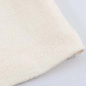 Detailed macro view of the double-stitched hem on a cream knitted cotton sleeveless top