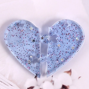 Detail of light blue heart puzzle resin earrings with embedded sequins and stars