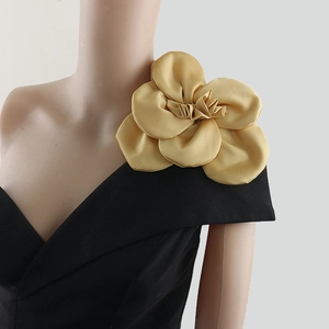Detailed close-up of a 3D satin fabric gold camellia flower brooch on a mannequin's shoulder
