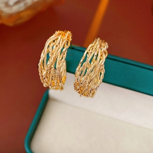 Macro shot of gold-plated twisted hoop earrings on a dark velvet jewelry box edge