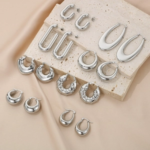 Collection of polished silver U-shape and hoop earrings on beige textured stones