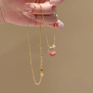 Close-up of gold-plated necklace with pink heart pendant and beaded chain detail
