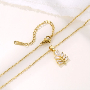 Golden titanium steel necklace with zircon cedar leaf pendant on a white fabric surface
