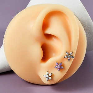 Three flower-shaped stainless steel opal labret studs displayed on a model ear