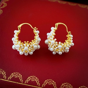 Detail shot of gold-plated hoop earrings with pearl embellishments on a red jewelry box
