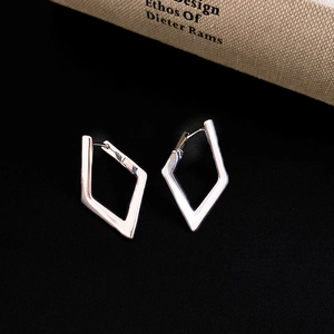 Detail shot of silver geometric diamond-shaped earrings on a black textured surface