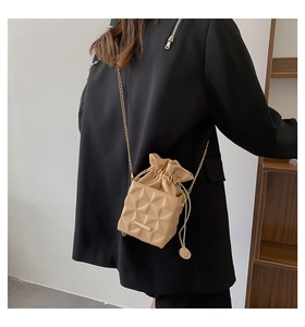 Detail of beige drawstring bucket bag with geometric texture and gold chain on model