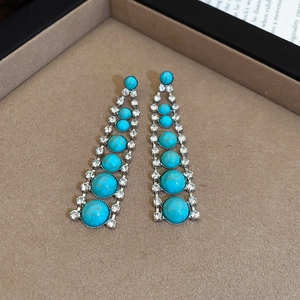 Détail de boucles d'oreilles argentées avec pierres turquoise et strass sur présentoir