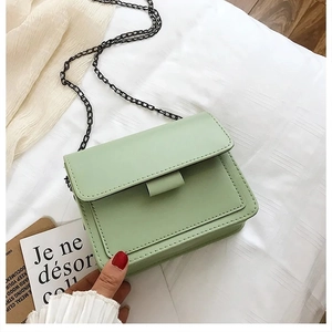 Detail of mint green crossbody bag with black chain strap on white fabric background