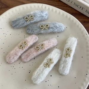 Close-up of plush bow hair clips with rhinestones in grey, pink, and white colors