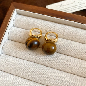 Macro detail of tiger eye stone bead earrings with golden clasp in a velvet jewelry box