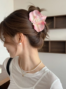 Floral hair clip with pink orchid ribbon, pearl earrings, and layered necklace on a model