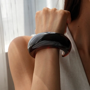 Detail of a dark red translucent resin wide bangle worn on a woman's wrist in soft indoor light