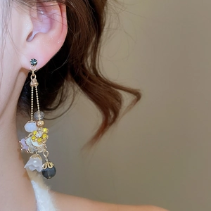 Close-up of elegant gold long drop earrings with blue floral beads on a female model