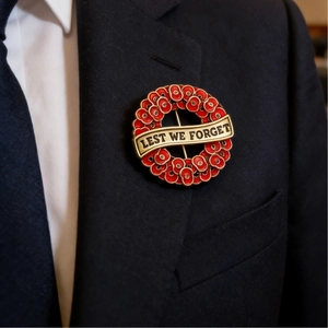 Red enamel poppy wreath brooch with Lest We Forget inscription on a navy blue blazer lapel