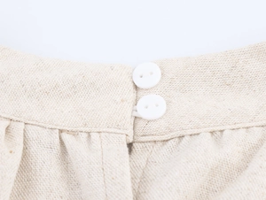 Detail eines beigen Leinenkleids mit Kokos-Stickerei, Doppelknöpfen und plissierter Taille