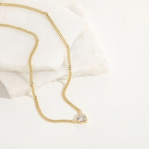 Macro detail of golden heart-shaped zircon pendant on a delicate chain necklace