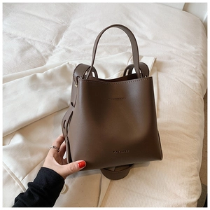 Brown leather bucket bag with embossed logo and adjustable shoulder strap carried by hand