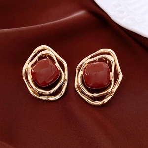 Detail of vintage irregular gold earrings with deep red square stones on red fabric