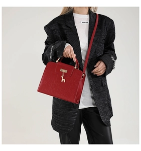Detail of red croc-embossed handbag with gold deer charm and chain handle worn by model