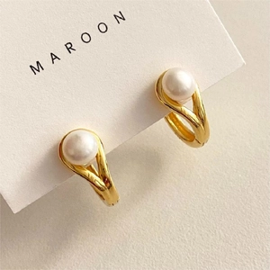 Macro view of golden V-shape intertwined earring featuring a round white pearl detail
