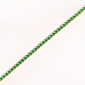 Macro detail of gold tennis necklace with round-cut emerald green stones on white background