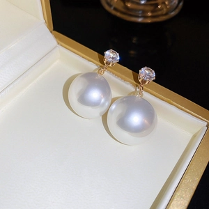 Détail de boucles d'oreilles dorées avec perles blanches et zircons dans un écrin à bijoux