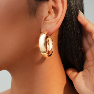 Golden chunky geometric hoop earrings with polished metallic finish worn by a model