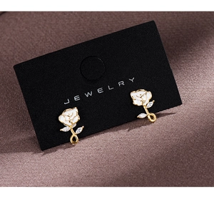 Close-up of vintage rose stud earrings with white petals and gold edges on black card