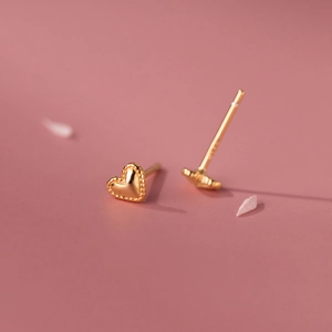 Macro shot of gold heart stud earrings with beaded edge details on pink background