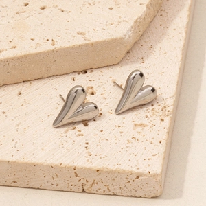 Macro detail of silver heart-shaped stainless steel earrings on natural travertine stone