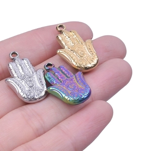 Pendentifs Main de Fatma en or, argent et irisé présentés sur la main pour l'échelle