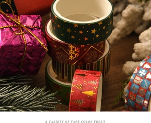 Macro shot of assorted Christmas washi tapes with festive foil patterns on silk and pine background