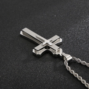 Detail shot of multi-layered silver cross pendant with textured rope chain on dark grey surface