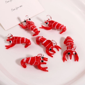Detail of six handmade red glass crayfish pendants with white stripes on a ceramic plate
