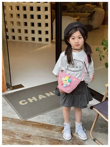 Pink woven crossbody bag for kids featuring colorful floral charms shown on child model